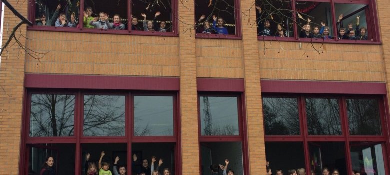 Kinder winken aus den Fenstern eines Schulgebäudes